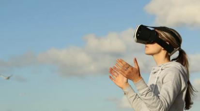 Ein Frau mit einer VR-Brille unter einem strahlend bleuen Himmel 