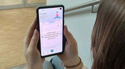 Eine Studentin hält ihr Handy, auf dem eine Seite der App zu sehen ist.