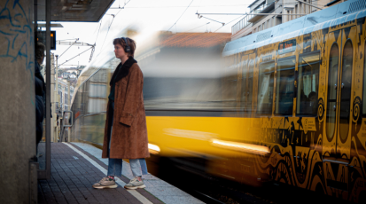 Eine Frau steht am Bahnsteig, rechts fährt eine Bahn vorbei