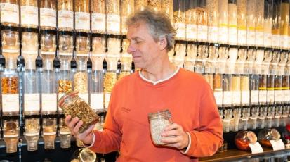 Ein Mann hält zwei Gefäße in der Hand. Im Hintergrund sind Lebensmittelschütten.