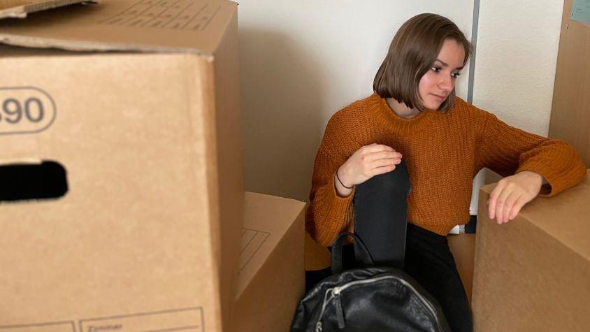 Eine junge Frau sitzt in ihrer Wohnung zwischen Umzugskartons. (Symbolbild) 