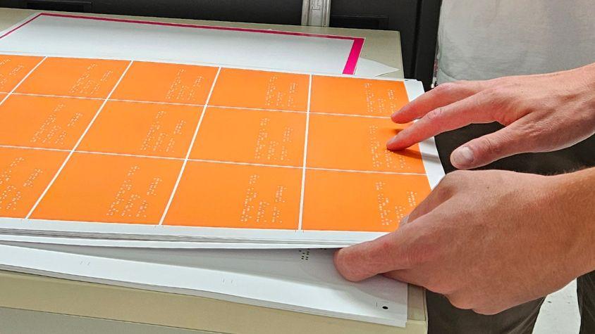 Eine Hand fühlt über die Braille-Schrift auf orangenen Postkarten