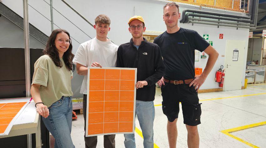 Das Team hinter "Dot Printing" in der Druckerei Burger mit orangenen Postkarten