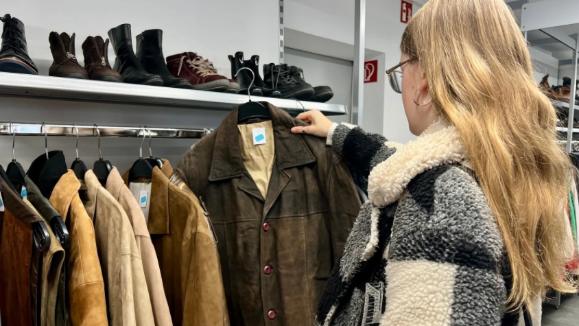 Ein Mädchen hält eine braune, Lederjacke in einem Secondhand-Laden in der Hand