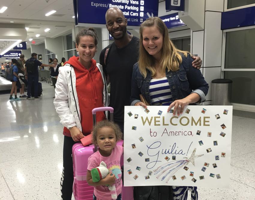 Ich stehe neben meinen Gasteltern im Flughafen, vor mir meine kleine Gastschwester. Meine Gastmutter hält ein Schild, auf dem "Welcome to America Giulia" steht.