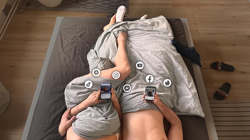 Zwei Menschen liegen zusammen im Bett und lenken sich mit Rating-Apps vom Wesentlichen ab