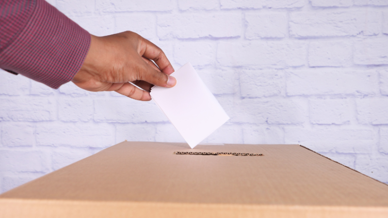 Eine Hand steckt einen Wahlzettel in den Kasten