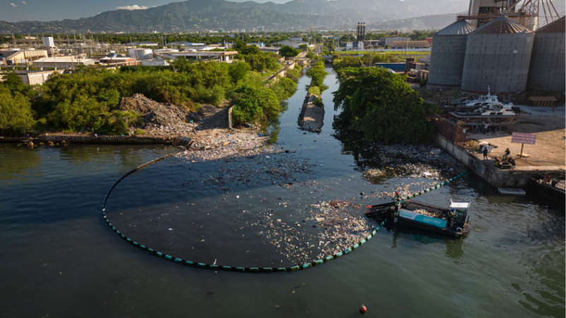 Drohnenaufnahme: Fluss mit Müll und Barriere